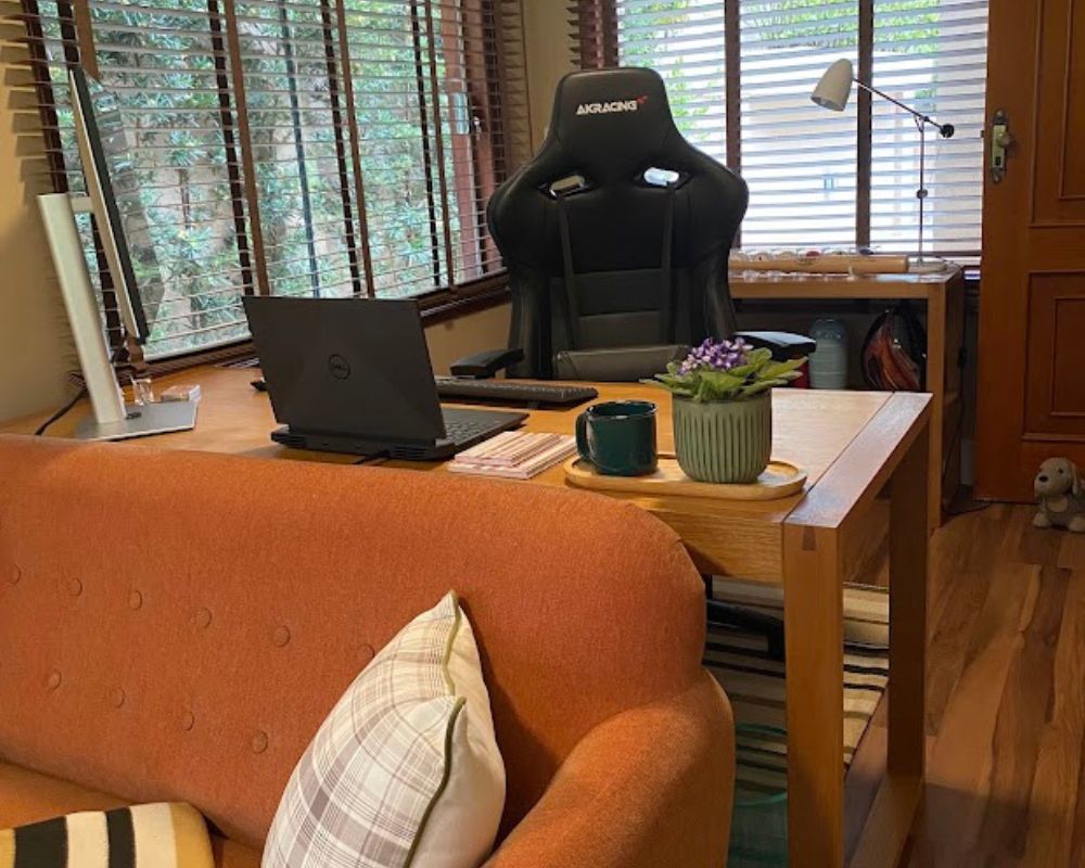 Sala de estar e escritório integrados com janelas amplas, persianas de madeira e vista para o jardim externo.