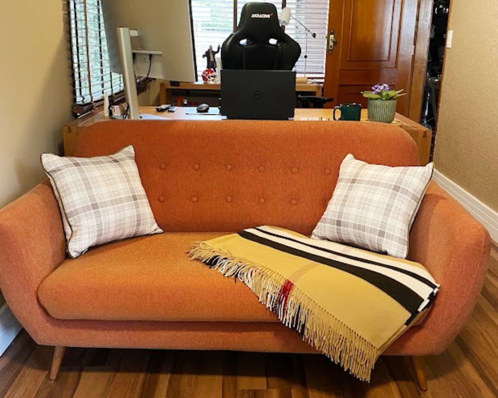 Sofá cor terracota com almofadas xadrez e manta bege, estilo farmhouse sofisticado em escritório.