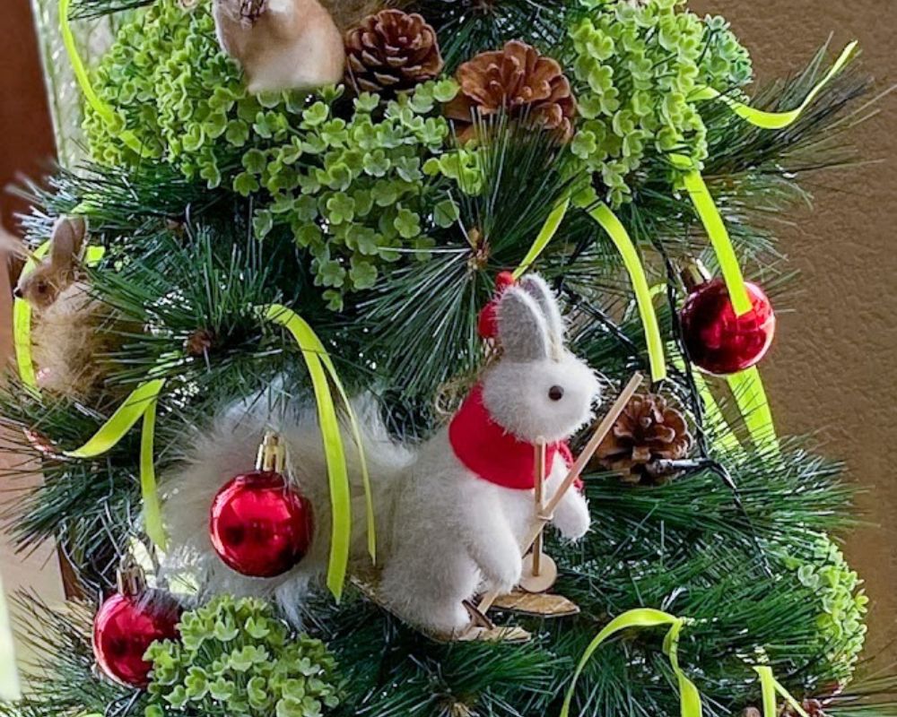 Árvore de Natal decorada com esquilo branco esquiador, bolas vermelhas e pinhas.